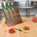 A Mercer Culinary Millennia knife set with green handles on a wooden board next to tomatoes.