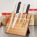 A Mercer Culinary acacia magnetic knife rack holding knives on a wood surface.