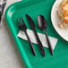 A green tray with black plastic utensils and a white napkin.