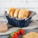 An oval Tablecraft rattan bread basket with bagels and strawberries inside.