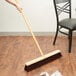 A person sweeping a restaurant floor with a Carlisle 24" push broom.