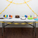 A table with a cake and cups on it with School Bus Yellow streamers hanging from the ceiling.