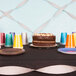 A table with a black tablecloth and a cake with silver streamers on it.