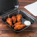 A white foam container with Genpak SN240-BK Black Foam Hinged Lid Container filled with fried chicken and dipping sauce.