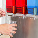 A person using a Crathco Mini-Quad beverage dispenser to pour red, blue, and green liquid into cups.