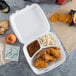 A Dart white foam three-compartment takeout container with chicken wings, chips, and a drink inside.