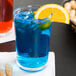 A Libbey Puebla tumbler filled with a blue drink with ice and an orange slice.