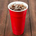 A red GET SC-32-R plastic tumbler filled with ice on a wooden table.