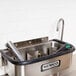 A stainless steel Nemco ice cream dipper well with a black and green faucet.