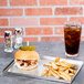 An American Metalcraft stainless steel tray with a sandwich and fries on it next to a glass of soda.
