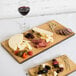 An American Metalcraft carbonized bamboo serving board with cheese and food on it, on a table with a glass of red wine.