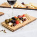 An American Metalcraft carbonized bamboo serving board with cheese, olives, and grapes on a table.