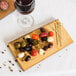 An American Metalcraft carbonized bamboo serving board with food on it next to a glass of wine.