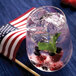 A glass of water with ice, berries, and mint on the rim.