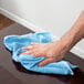 A hand using a blue Unger SmartColor cloth to wipe a table.