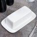 A white porcelain butter dish with a cover on a table.