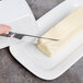 A knife cutting a piece of butter on a white plate with a 10 Strawberry Street Classic White porcelain butter dish cover.
