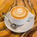 A 10 Strawberry Street white porcelain coffee cup filled with coffee with a heart design in the foam on a counter.