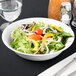 A 10 Strawberry Street white porcelain vegetable bowl filled with salad with vegetables and a fork.