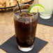 A Libbey customizable cooler glass of brown liquid with ice and a lime wedge.
