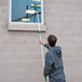 A man using an Unger telescopic pole to clean a window.