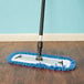 A Lavex blue microfiber mop with a handle and blue fringe on a wood floor.