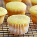 A group of Hoffmaster white fluted baking cups on a wire rack filled with lemon cupcakes.