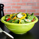 A green plastic salad bowl filled with salad and a fork.