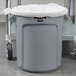 A grey Rubbermaid Brute trash can with a white bag inside.