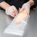 A person in a black glove using an ARY Vacmaster full mesh plastic bag to hold a piece of cheese.