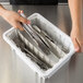 A hand using tongs to put silverware in a white Metro Divider Tote Box.