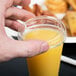 A hand putting a clear plastic lid with a straw slot on a plastic cup of orange juice.