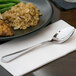 A 10 Strawberry Street Lincoln stainless steel dinner spoon on a napkin next to a plate of food.