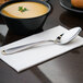 A 10 Strawberry Street Parisian stainless steel dinner spoon on a napkin next to a bowl of soup.