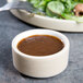 A Chef & Sommelier stoneware ramekin filled with brown sauce next to a salad plate.