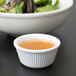 A bowl of salad with a white fluted ramekin of sauce.