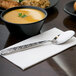A bowl of soup with a 10 Strawberry Street Dubai stainless steel dinner spoon on a napkin.