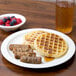 A Carlisle white polycarbonate plate with a waffle, sausage, and berries on it.