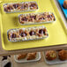 A yellow Cambro fiberglass market tray on a table with pastries and muffins.
