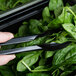 A person using Cambro black plastic tongs to serve spinach from a bowl.