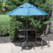 A table with a blue Grosfillex umbrella on it and chairs.