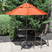 An outdoor patio table with an orange Grosfillex umbrella on an aluminum pole.
