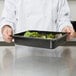 A chef holding a Cambro black polycarbonate food pan with salad in it.