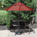 A table and chairs under a red Grosfillex umbrella with a metal base.