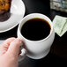 A hand holding a white Cambro contoured mug full of coffee.