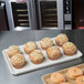 A MFG Tray eggshell fiberglass supreme display tray of muffins on a counter.