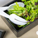 A Tablecraft black melamine bowl filled with salad on a table.