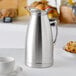 A silver stainless steel thermal beverage server on a table.