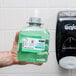 A hand holding a bottle of green liquid soap with a GOJO label.
