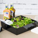 A salad in a black Tablecraft bowl on a table.